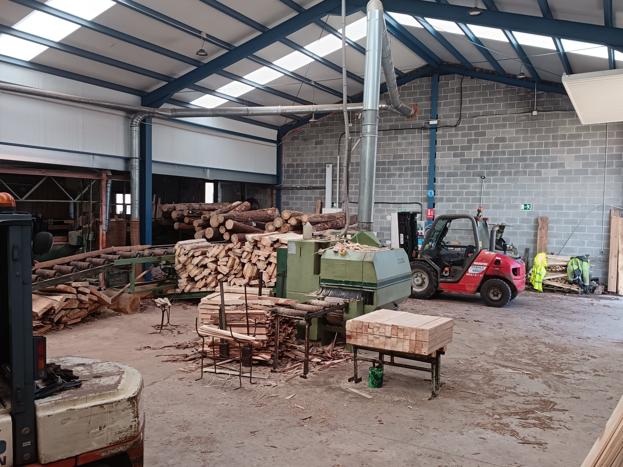 Vista general del interior del aserradero con maquinaria, troncos y carretilla elevadora