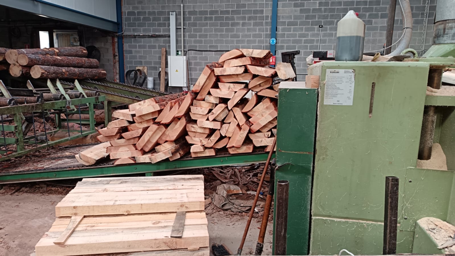 Madera reci&eacute;n cortada apilada sobre maquinaria en el interior del aserradero