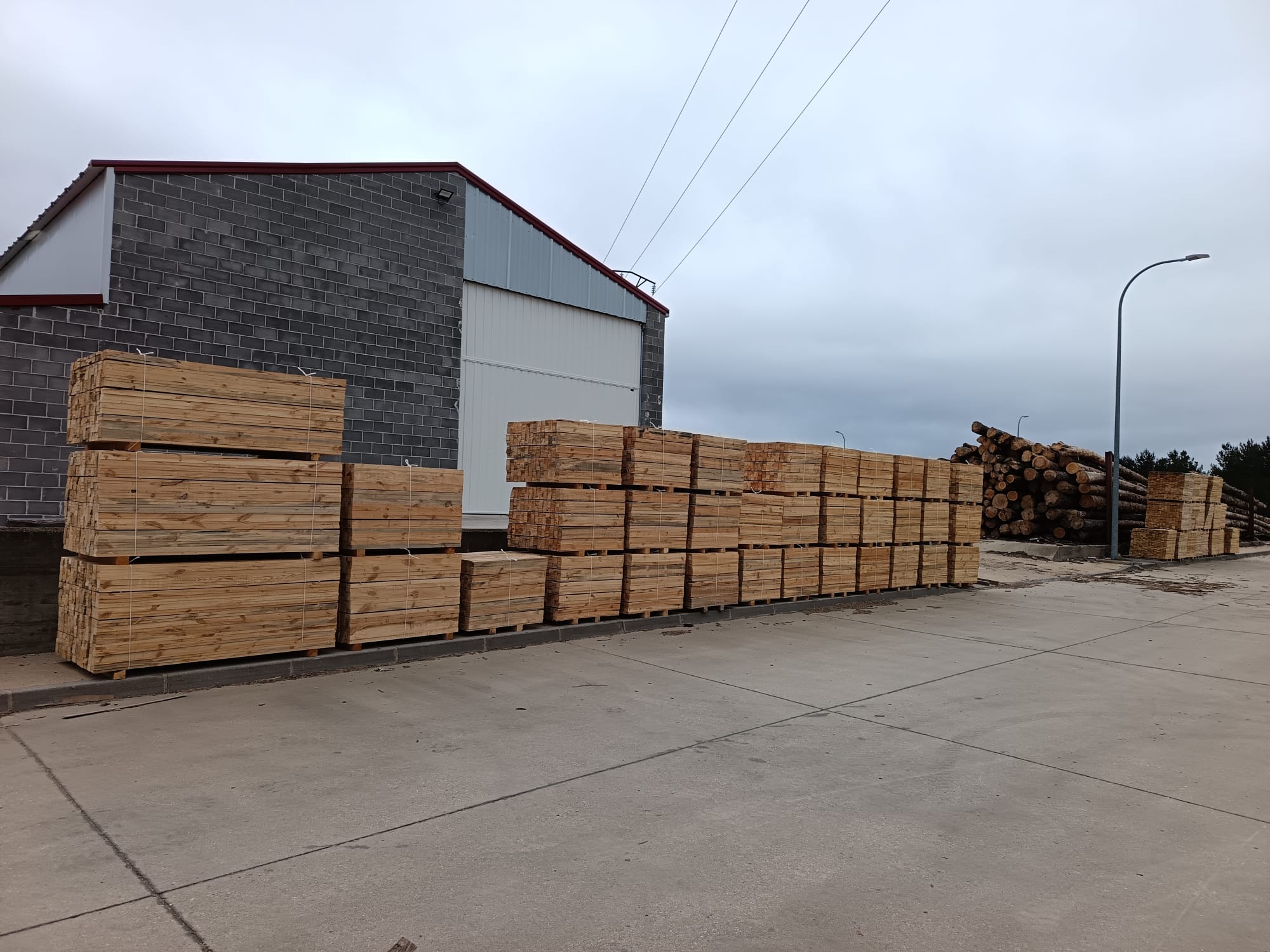 Apilado de tablones de madera en el exterior de una nave industrial